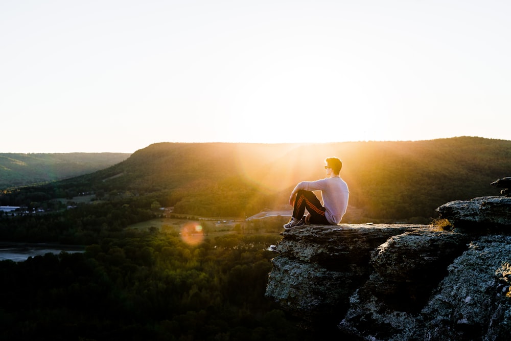 man sitting on rock near cliff with overlooking mountains