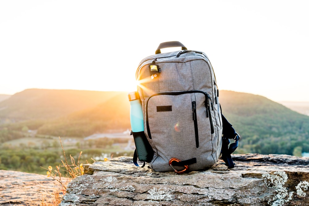 grey and black hiking backpack and cyan tumbler on grey rock during sunset