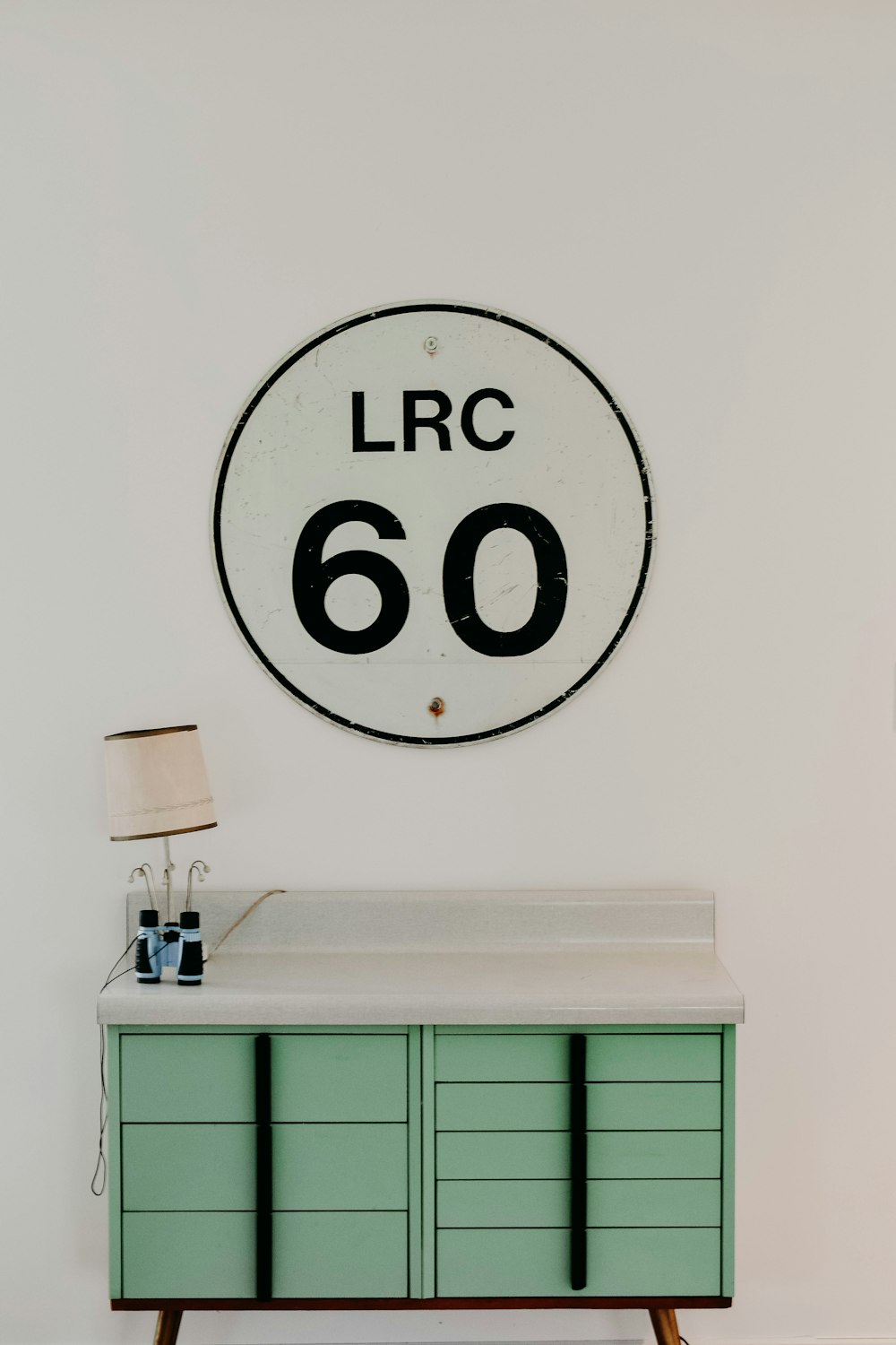 LRC 60の壁の看板の近くに茶色のランプシェードが付いた白と緑の木製デスク