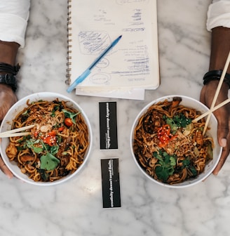 person holding two bowls of cooked foods