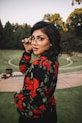 woman wearing black, green, and red floral long-sleeved top standing on park