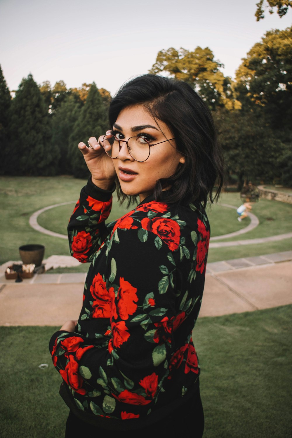 woman wearing black, green, and red floral long-sleeved top standing on park