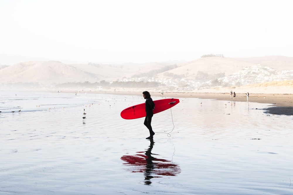 person on body of water carrying red surfboard