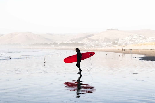 person on body of water carrying red surfboard in Morro Bay United States