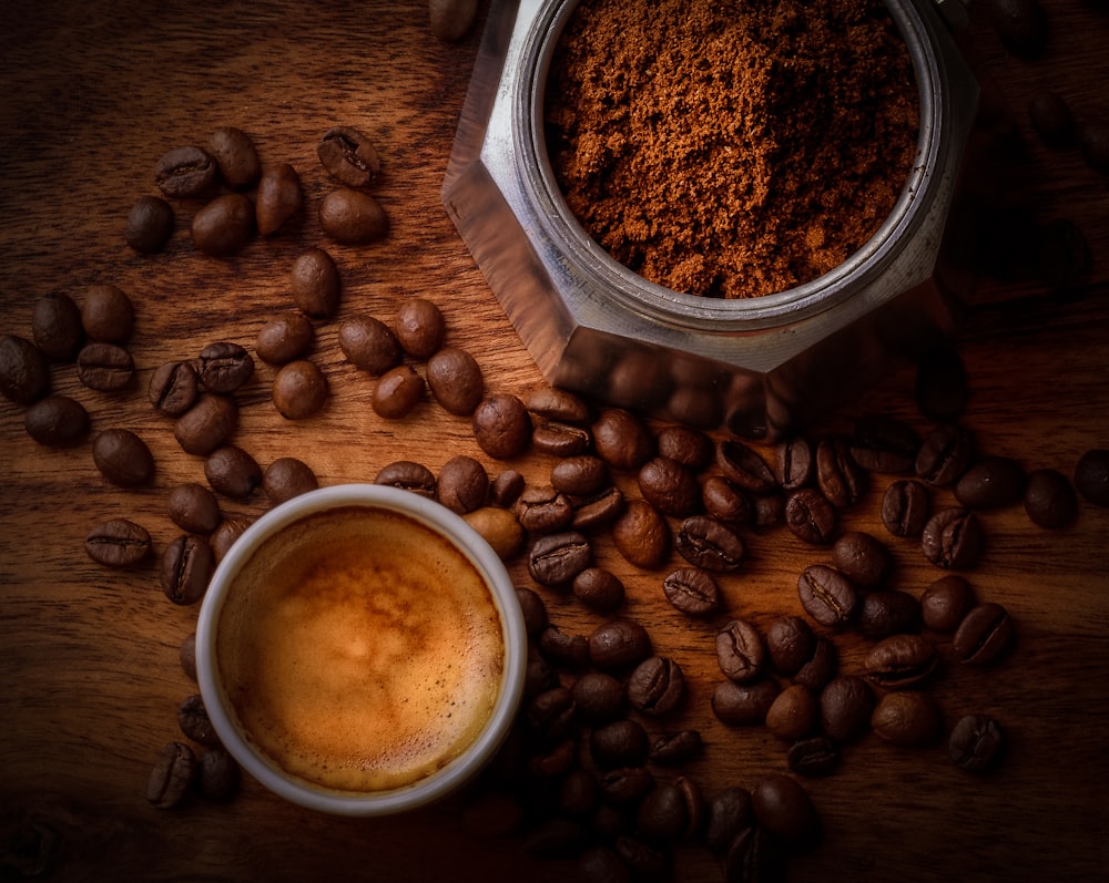 granos de café marrón junto a una taza de cerámica blanca