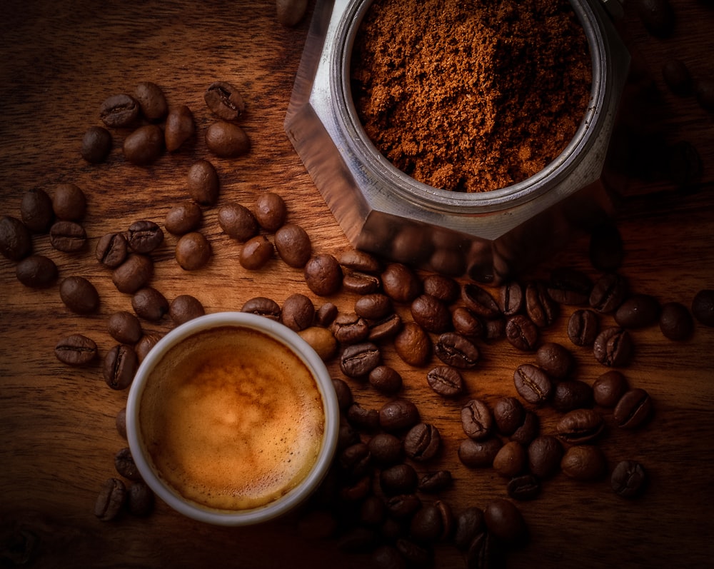 brown coffee beans beside white ceramic mug