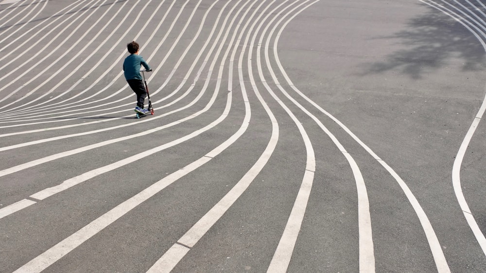 회색 콘크리트 포장 도로에서 킥 스쿠터를 재생하는 소년