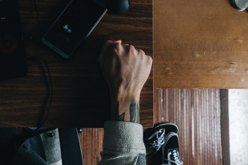 person's fist beside smartphone on brown table