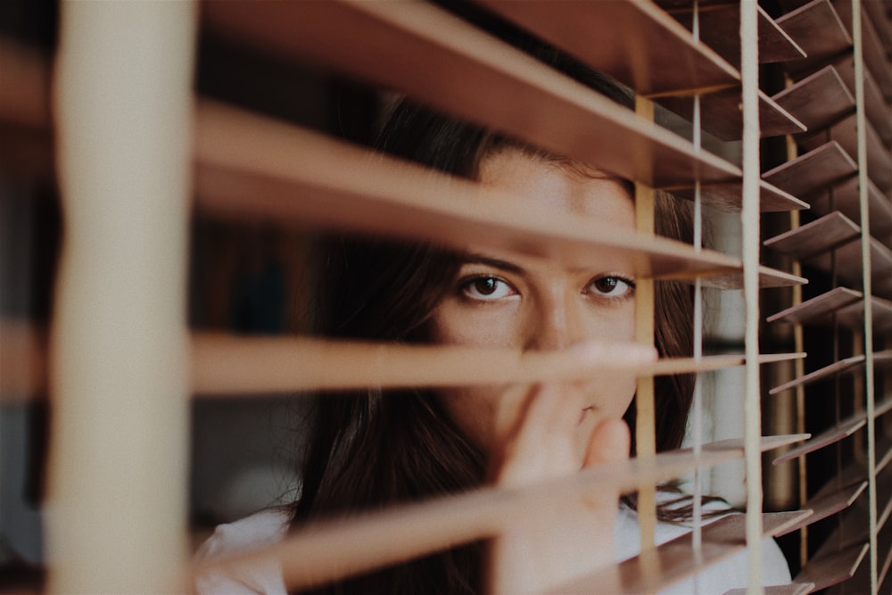 woman peeking over window blinds