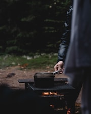 A rugged outdoor scene showing a titanium seed plate resting safely on rocks beside a campfire.