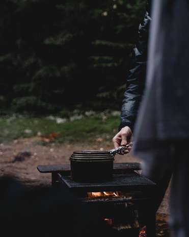 A rugged outdoor scene showing a titanium seed plate resting safely on rocks beside a campfire.