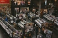 A vintage-style record store filled with rows of vinyl records and CDs. People are browsing through the music collections, with walls adorned with posters and album art. The setting appears spacious, with a cozy and nostalgic ambiance.