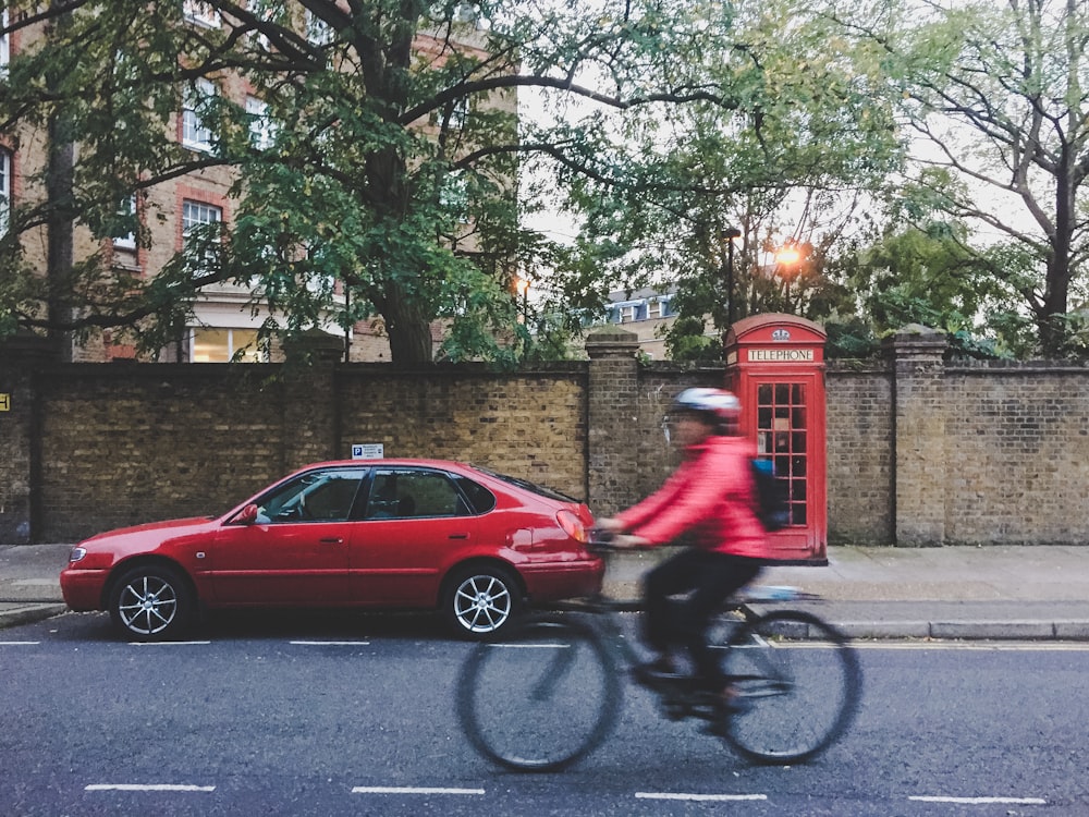 빨간 세단과 전화 부스 근처에서 자전거를 타는 사람의 타임 랩스 사진