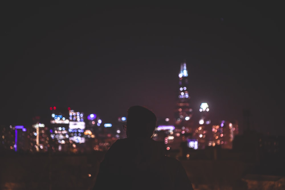 silhouette of man facing lighted concrete buildings