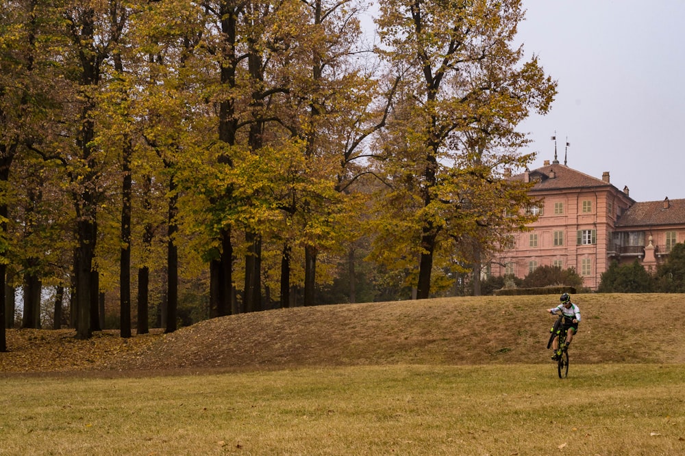 昼間、木の近くの緑の芝生で自転車に乗る男性