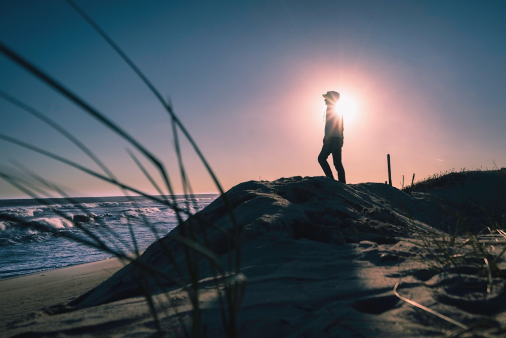 silhouette selective focus photography of person standing on beach facing body of water during daytime