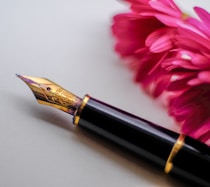 black and gold-colored fountain pen beside flower