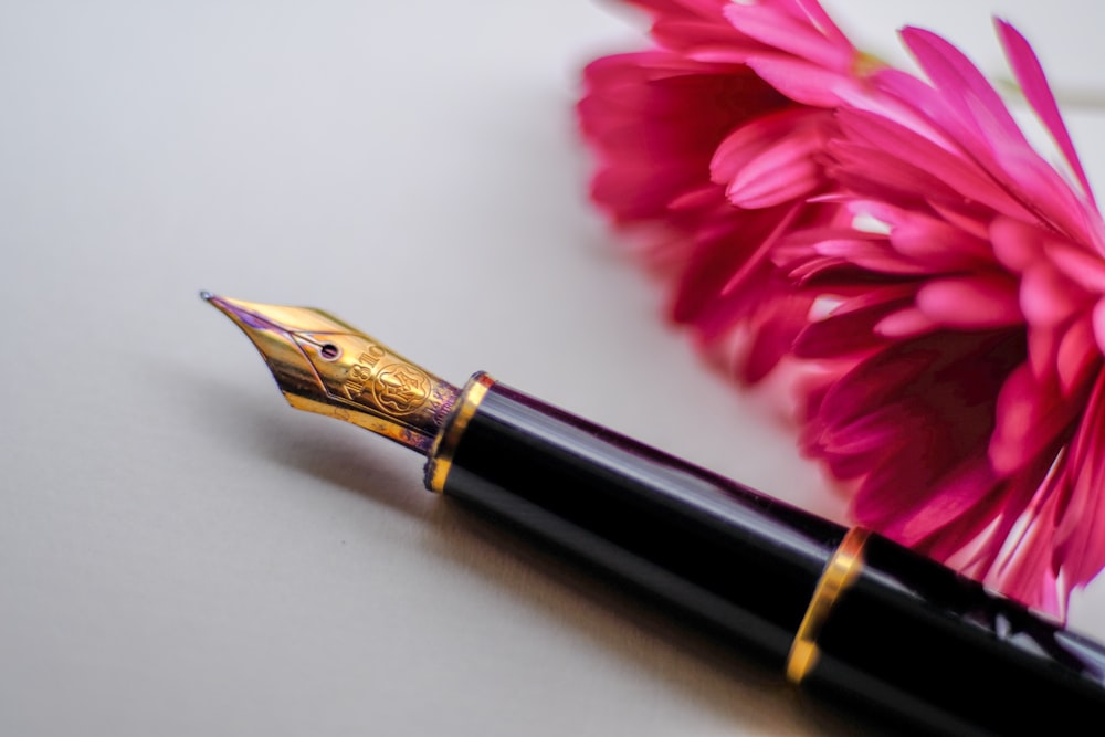 black and gold-colored fountain pen beside flower