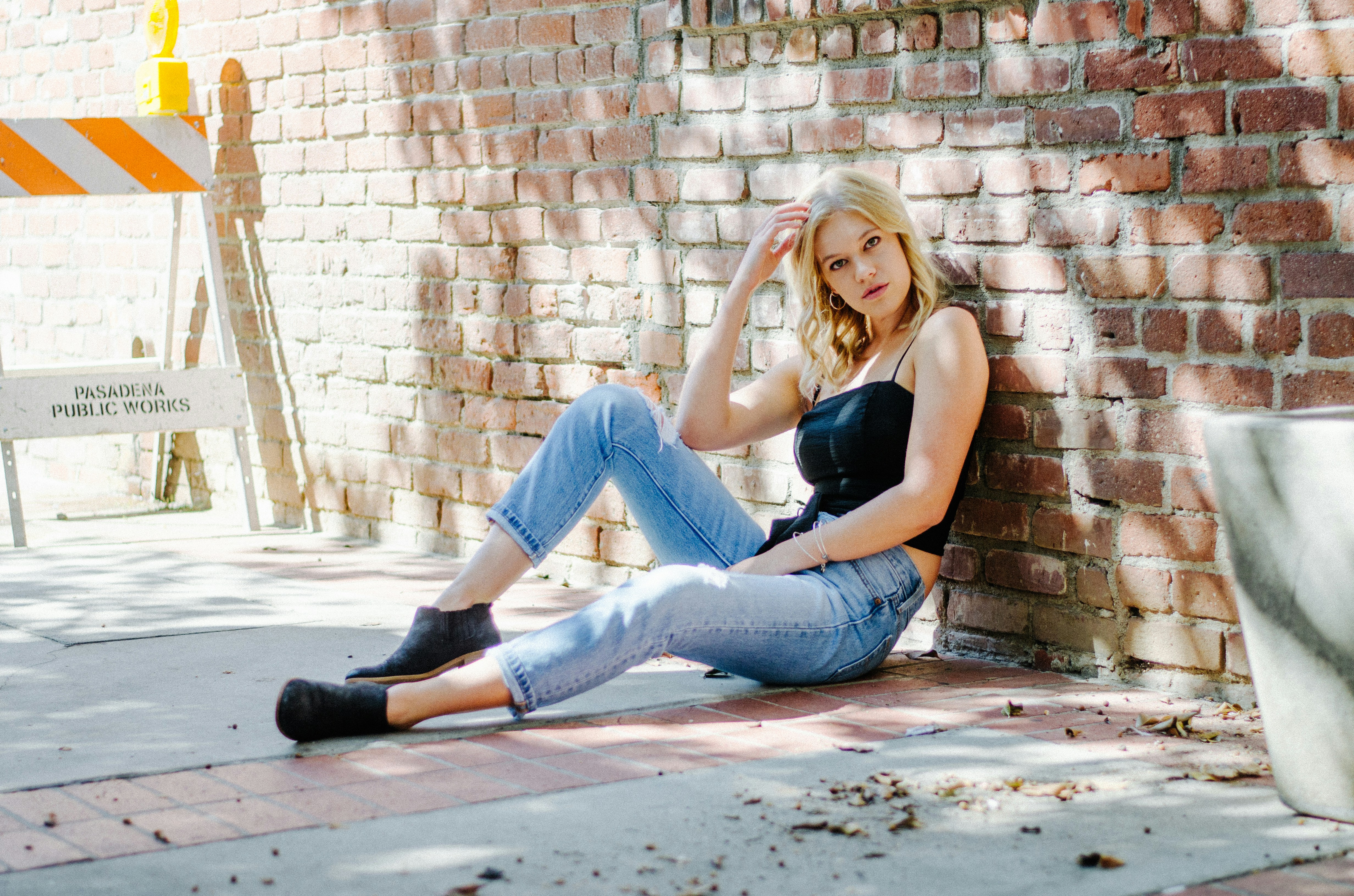 woman holding her hair sitting beside brown brick wall female teams background