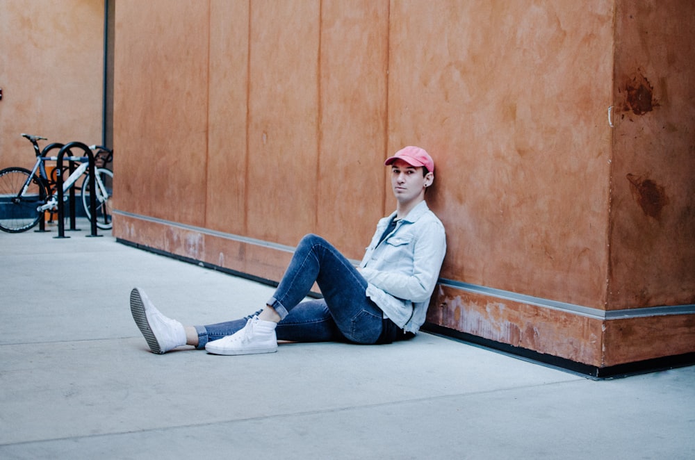 man sitting on floor while leaning on brown wall