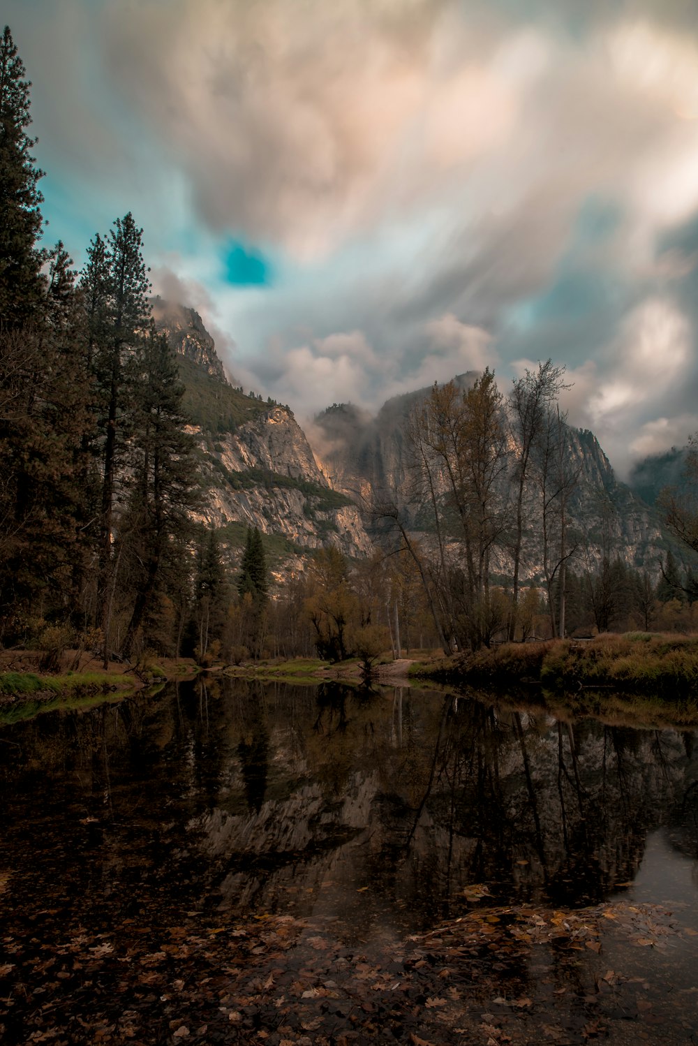 glacier mountain beside pine trees reflection on body of water under gray cloudy sky at daytime