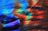 A dynamic swirl of vibrant colors including blue, red, green, and orange creates an abstract and fluid visual experience. The interplay of light and color resembles brush strokes in a painting, evoking a sense of movement and energy.