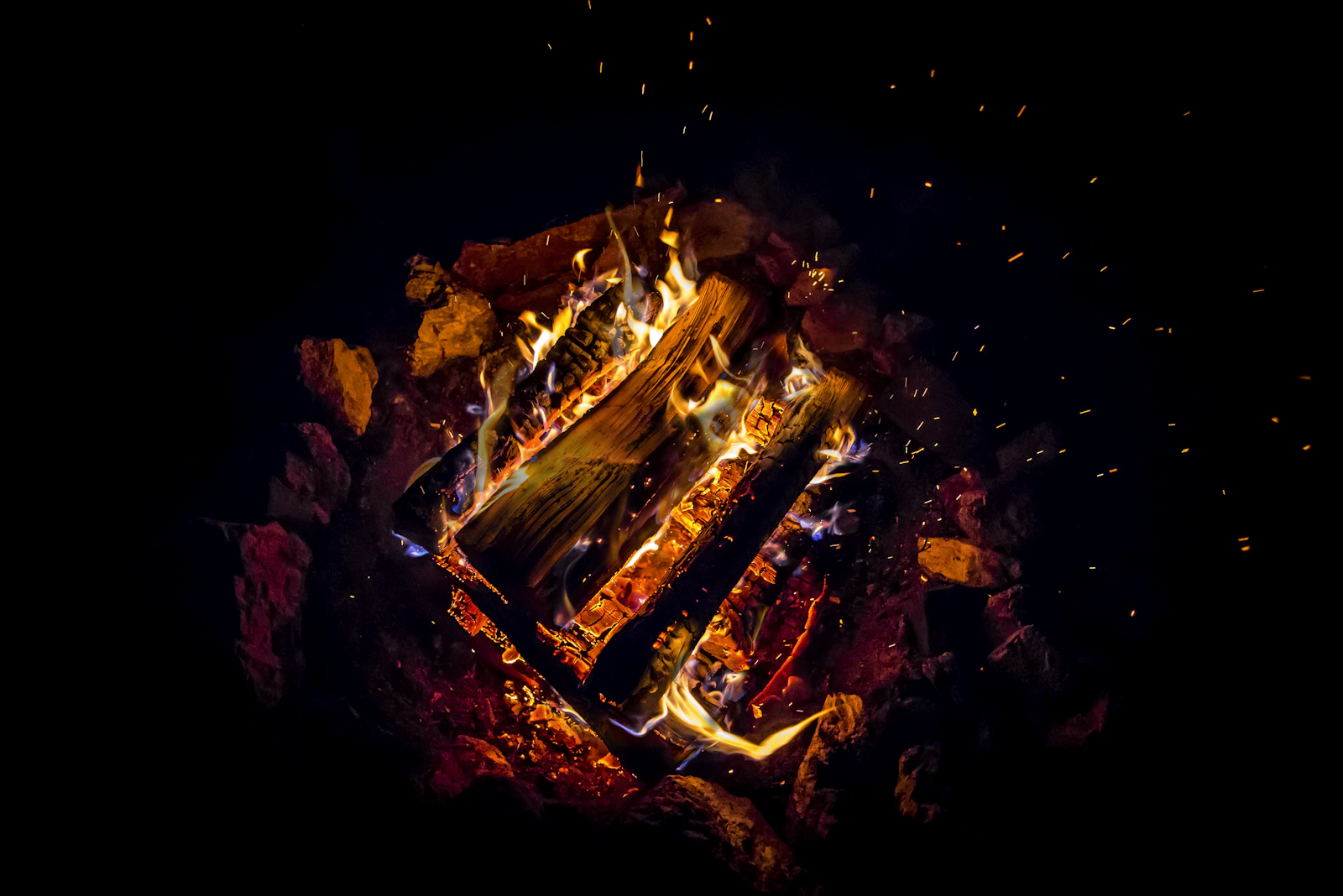 A campfire burning bright against the dark, embers rising into the night