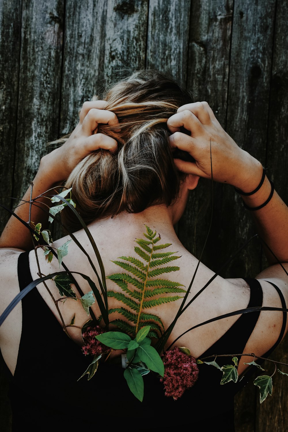 woman in black tank top with red petaled flower and assorted leaf on her back