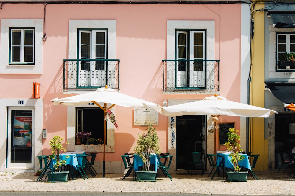 dois guarda-sóis brancos do pátio perto do edifício de concreto pintado de rosa e branco