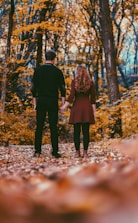 A warm photo of a couple holding hands outdoors, surrounded by fall leaves.