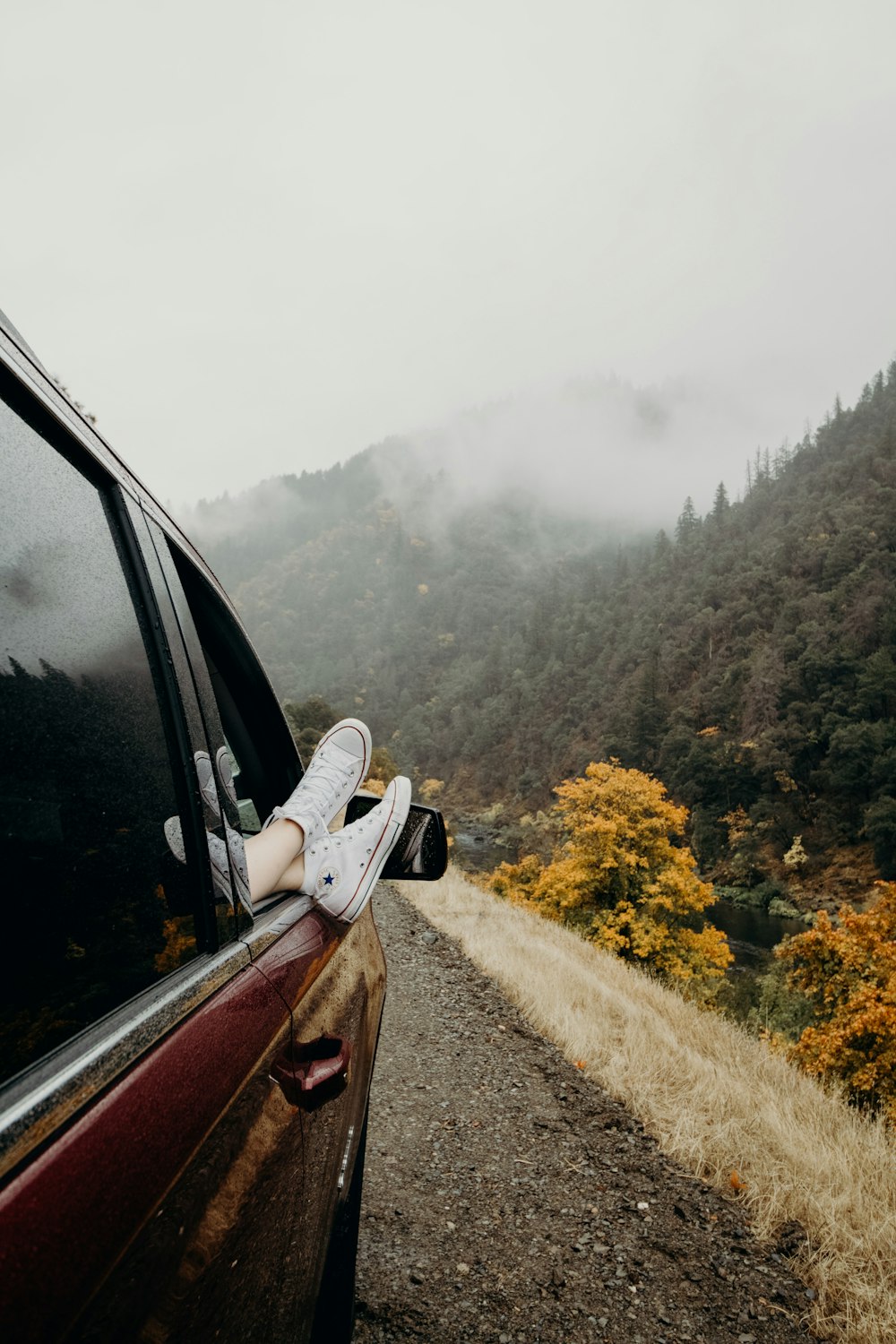 person's feet wearing white Converse sneakers on car door