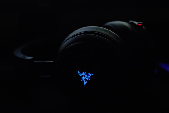 A pair of over-ear headphones with a glowing blue logo. The background is dark, emphasizing the illuminated logo.