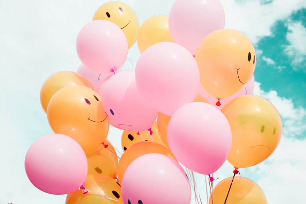 Pink and orange balloons in sky. Orange balloons have smiley faces. 