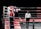 A boxing match in progress features two fighters inside a ring, one wearing red gear and the other in blue. The referee stands close by, ensuring the match proceeds fairly. The ring is equipped with ropes and padded corners, set against a black background, highlighting the intense action taking place.