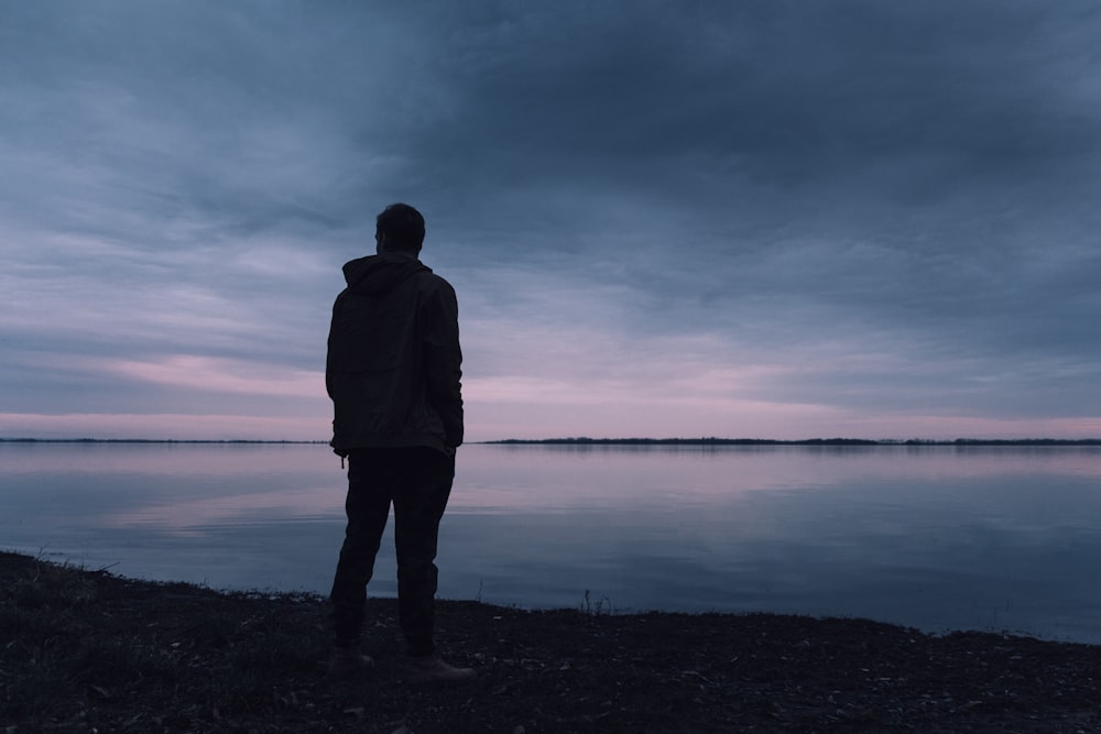 silhouette of man standing near body of water