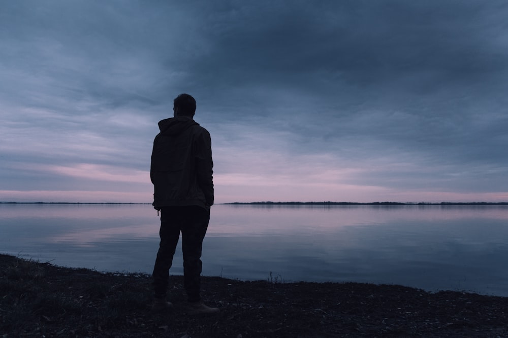 silhouette di uomo in piedi vicino allo specchio d'acqua