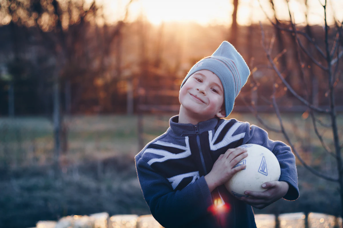 Smiling boy outdoors holding a soccer ball at sunset
