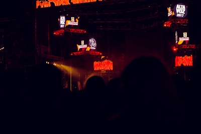 The image captures a dark concert or festival setting featuring illuminated screens displaying the text 'Alta Voz 2017'. The scene includes stage equipment and what appears to be a large outdoor event with colorful lighting effects.
