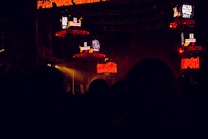 The image captures a dark concert or festival setting featuring illuminated screens displaying the text 'Alta Voz 2017'. The scene includes stage equipment and what appears to be a large outdoor event with colorful lighting effects.