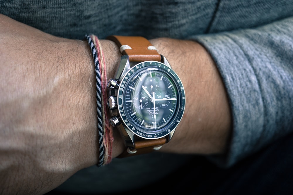 person wearing round silver-colored bezel chronograph watch with brown leather strap