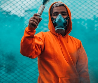 man wearing orange pullover hoodie holding smoke flare