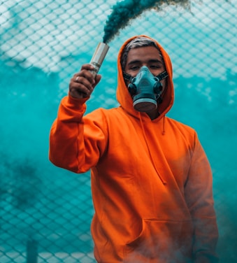 man wearing orange pullover hoodie holding smoke flare