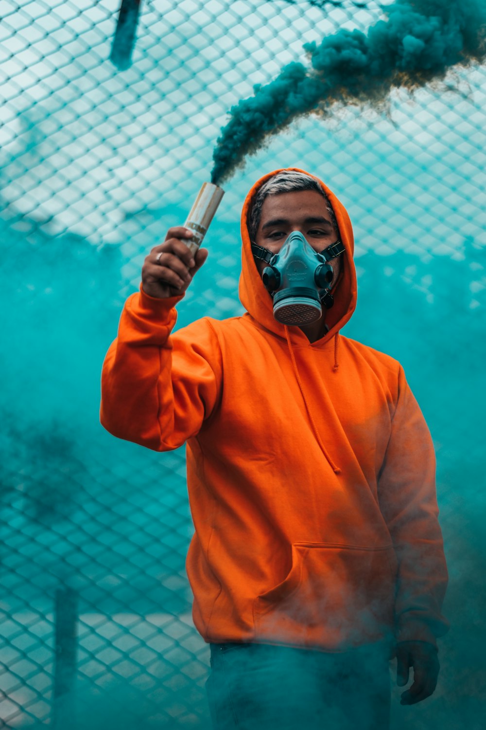 man wearing orange pullover hoodie holding smoke flare