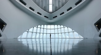 A modern and minimalistic interior with a futuristic architectural design. The space features curved lines and large windows that allow natural light to illuminate the area. The reflection on the glossy floor adds depth to the scene.