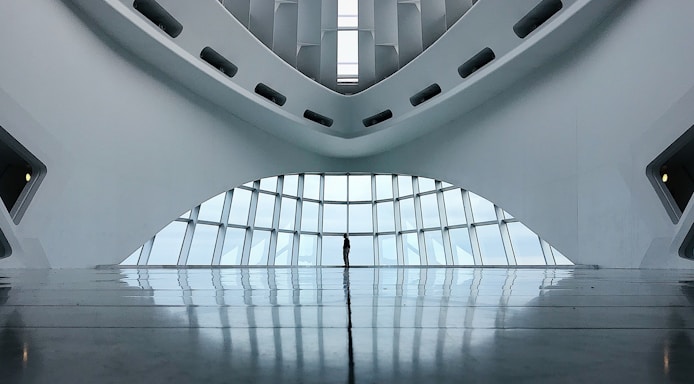 A modern and minimalistic interior with a futuristic architectural design. The space features curved lines and large windows that allow natural light to illuminate the area. The reflection on the glossy floor adds depth to the scene.