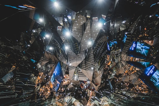 A complex, futuristic interior design featuring reflective surfaces and angular patterns creating a kaleidoscopic effect. Various advertisements and lights are visible, adding to the vibrant and chaotic atmosphere.