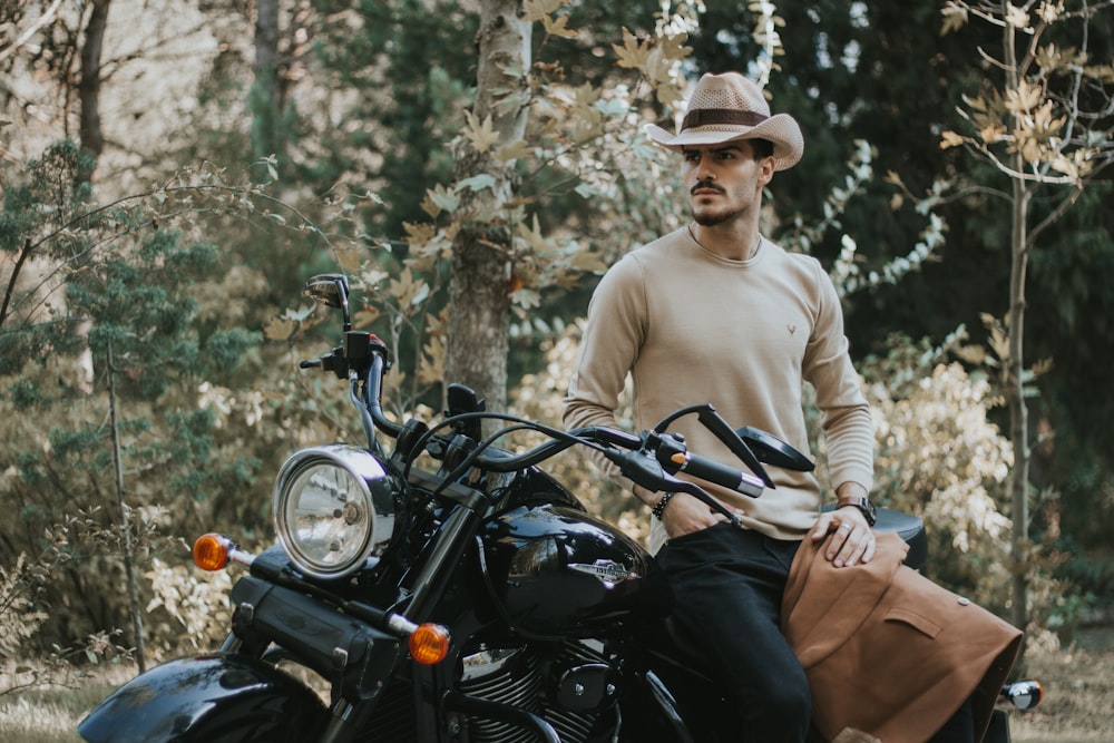 man sitting on black motorcycle besides trees at daytime