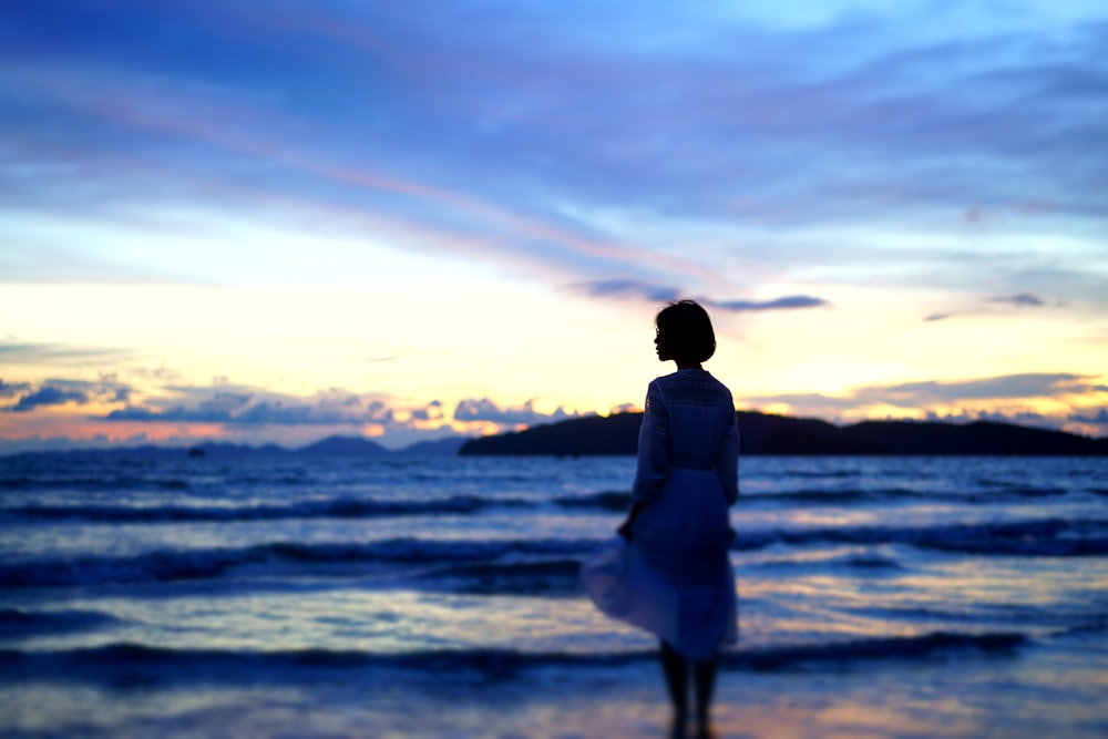 silhouette photography of woman standing on shore during golden hour