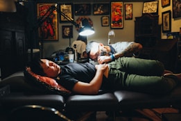 man in gray polo shirt tattooing a man
