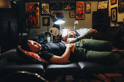 man in gray polo shirt tattooing a man